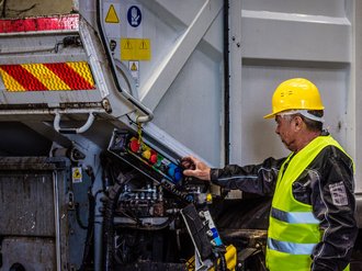 Mann bedient Knöpfe an einem Müllwagen