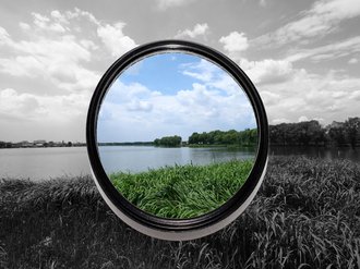 Blick auf Natur durch grau getöntes Glas mit rundem Ausschnitt in der Mitte.